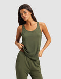 A woman in a Cozy Earth Women's Bamboo Stretch-Knit Lounge Tank stands against a light gray background, holding the hem of her olive green sleeveless top with one hand.|Color:Olive
